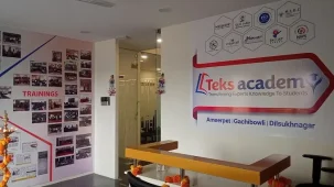 Alt text: Reception area of Teks Academy, a leading institute offering DevOps Course in Hyderabad, with the logo on the wall showing branches in Ameerpet, Gachibowli, and Dilsukhnagar, alongside a wall display of training photos.